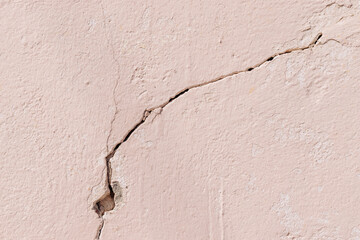 Close-up of crack on light pink plastered concrete wall
