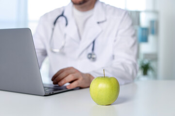 Nutritionist working with laptop at table in clinic, focus on green apple