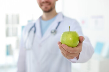 Nutritionist with green apple and stethoscope in clinic, selective focus