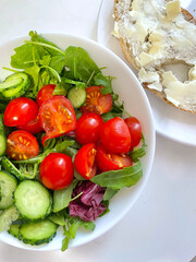 A bright salad of fresh vegetables with cherry tomatoes, cucumbers and lettuce, as well as a slice of bread spread with soft cheese, are ideal for a healthy diet.