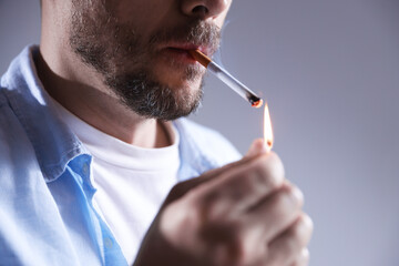 Man lighting cigarette with match on light background, closeup
