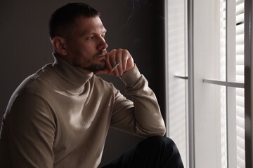 Man smoking cigarette near window in room