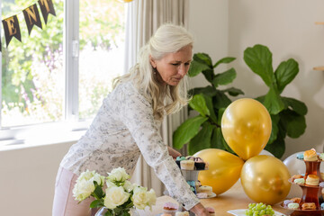 Senior woman arranging cupcakes on table at festive gathering with balloons