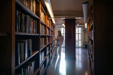 Woman reading a book in quiet library aisle with warm natural light
