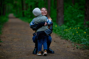 Fototapeta premium A joyful woman hugs a child on a forest path, sharing a heartfelt moment in nature. Surrounded by greenery and trees, they express love, warmth, and connection in an outdoor setting.