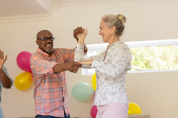 Senior friends dancing joyfully at home, celebrating with colorful balloons © wavebreak3