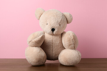 Cute teddy bear on wooden table against pink background