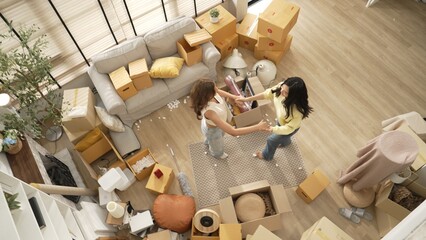 Happy lesbian lover dancing together at living room in moving day. Couple of friend moving to music and perform freestyle dancing at living room with cardboard box scattering. Relocation. Myrmidon.