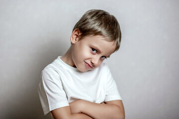 Naklejka premium Young boy in a white shirt with short hair, smiling mischievously with crossed arms; soft lighting enhances the playful, confident expression on his face