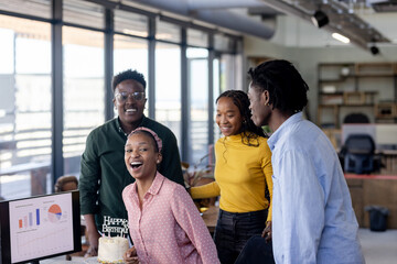 Colleagues celebrating birthday in modern office, smiling and enjoying cake together