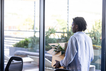 African American man carrying box with plant, moving into modern office space