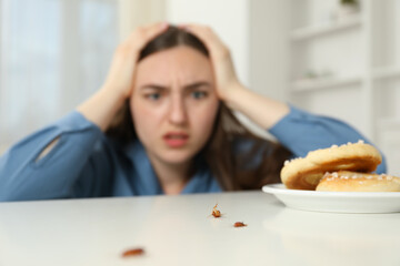 Shocked young woman looking at cockroaches and pretzels on white table indoors, selective focus....