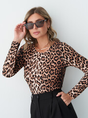 Woman in leopard print top, wearing sunglasses and gold earrings with wavy hair. She's posing...