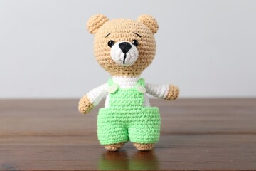 Cute knitted toy bear on wooden table against light background