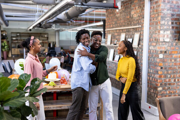 Celebrating in office, African American colleagues sharing joyful hugs and laughter