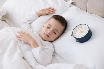 Bedtime. Cute boy sleeping and alarm clock in bed