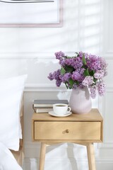 Bouquet of beautiful lilac flowers, coffee and books on nightstand