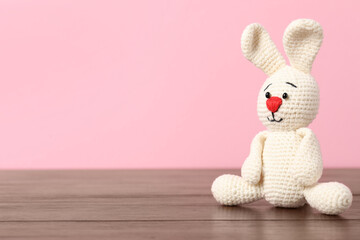 Fototapeta premium Cute knitted toy bunny on wooden table against pink background. Space for text