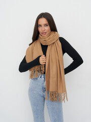 Stylish woman with long brown hair in black top and light jeans wearing a tan fringed scarf,...