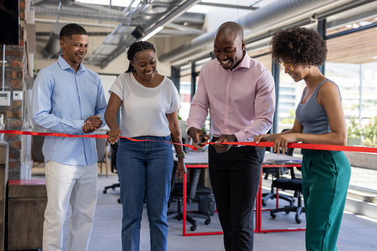 Celebrating office opening, diverse team cutting red ribbon with excitement - Powered by Adobe