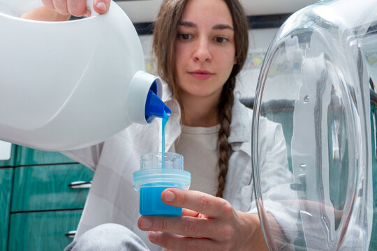 Focused Gen-Z Girl Pouring Blue Detergent into Measuring Cap