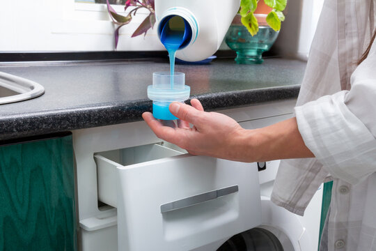 Young Woman Pouring Blue Detergent into Cap Before Laundry Load