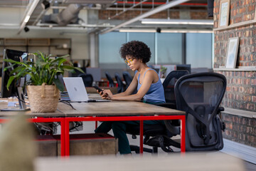Fototapeta premium African American woman using smartphone and laptop at modern office desk
