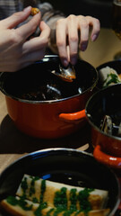 A woman is living in a luxurious restaurant, eating delicious fresh mussels in sauce from a red saucepan. Traditional Mediterranean cuisine.