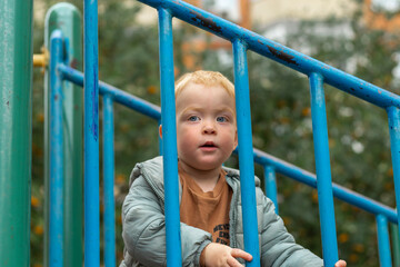 Obraz premium A little red-haired boy climbs the stairs on the playground and holds on to the handrail. Outdoor games