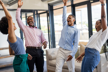 Colleagues celebrating success together in modern office, raising hands joyfully