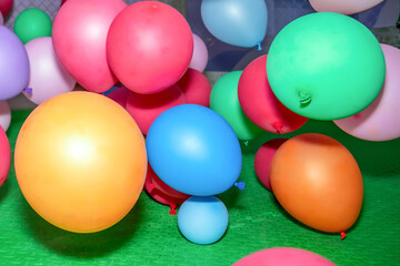 Colorful balloons of various sizes and shades, including red, green, blue, orange, and pink, clustered together in a playful arrangement. Shadows suggest a party or celebration atmosphere