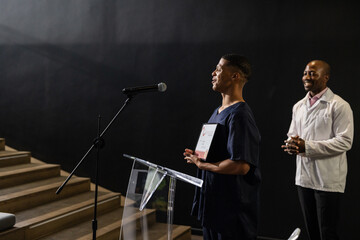 Receiving award on stage, African American man applauded by audience in auditorium
