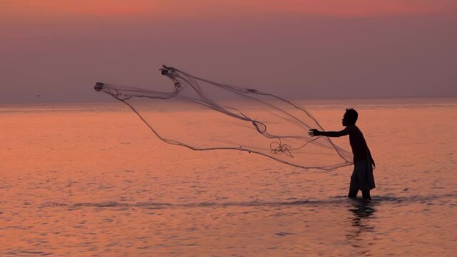 Sunset fisherman wades through calm waters to cast his net during twilight hours