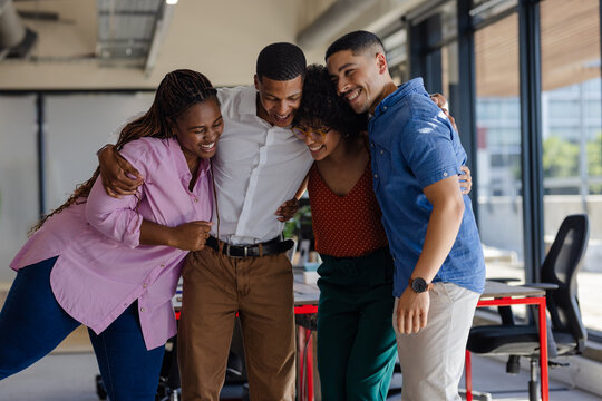 Diverse colleagues embracing and laughing together in modern office setting
