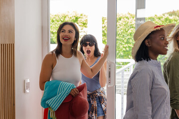 Women entering vacation home, carrying beach towels and hats, excited for getaway © WavebreakMediaMicro