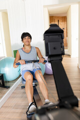 Fototapeta premium Woman exercising on rowing machine at home, smiling and staying fit