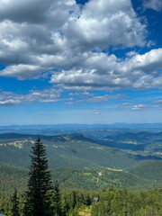 Fototapeta premium A stunning view of Ravna Planina from Mount Jahorina, with rolling green hills and rugged mountain peaks stretching into the distance.