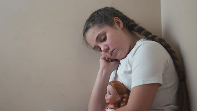 Young girl sitting on the floor with her doll. Girl punished with a doll in a corner. A teenage girl is traumatized by violence and psychological trauma. A young lifestyle girl is on the floor with.