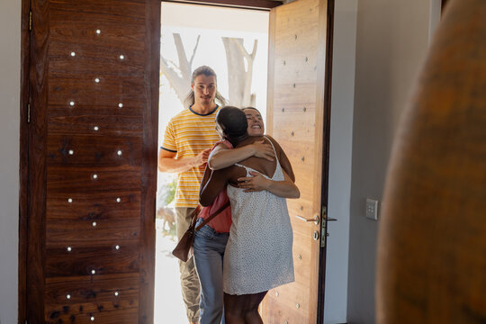 Friends greeting with warm hugs at home entrance, smiling and welcoming each other - Powered by Adobe