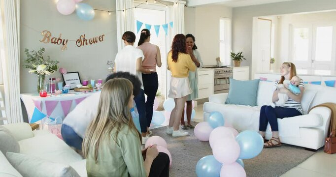 Group of happy multiracial and white female friends with baby talking and embracing at a baby shower