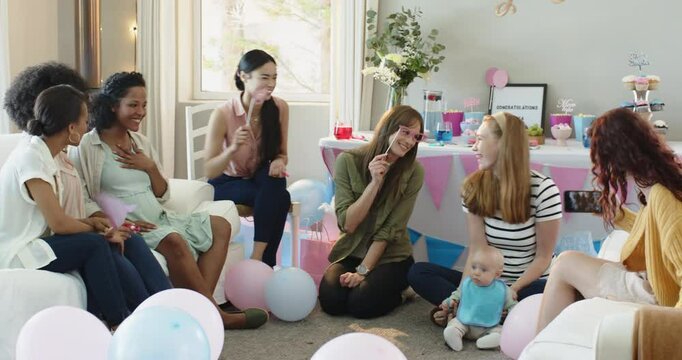 Group of happy multiracial and white female friends with baby taking pictures at a baby shower party