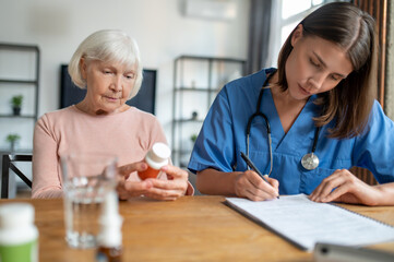Fototapeta premium Woman providing health care and assistance to aged patient offering treatment and medication