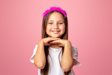 Childhood, beauty and fashion. Cheerful little girl with crown enjoys beauty, isolated on pink background, copy space