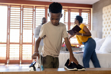 Young boy organizing shoes at home while parents preparing in background