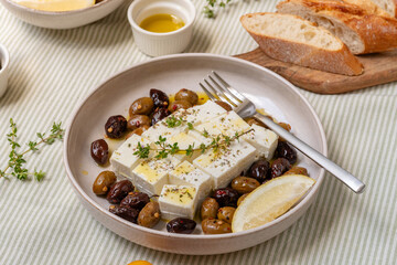 Fresh feta cheese with olives, olive oil and herbs with fresh bread, traditional Greek or Italian food, Mediterranean diet