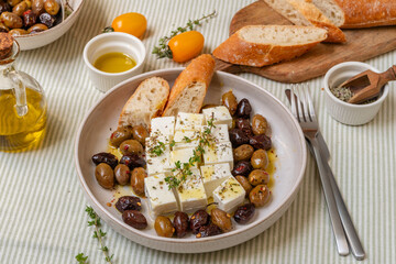 Freshly prepared feta cheese served on a plate with assorted olives, garnished with herbs and lemon slices and  crusty bread, traditional Greek or Italian food, Mediterranean diet
