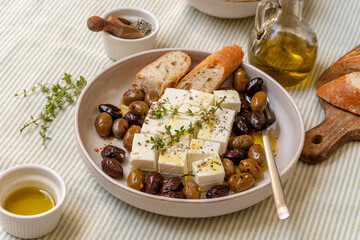 Freshly prepared feta cheese served on a plate with assorted olives, garnished with herbs and lemon slices and  crusty bread, traditional Greek or Italian food, Mediterranean diet