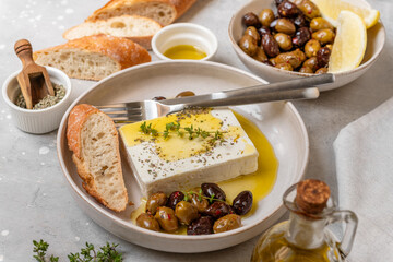 Fresh feta cheese with olives, olive oil and herbs with fresh bread, traditional Greek or Italian food, Mediterranean diet