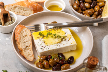 Fresh feta cheese with olives, olive oil and herbs with fresh bread, traditional Greek or Italian food, Mediterranean diet
