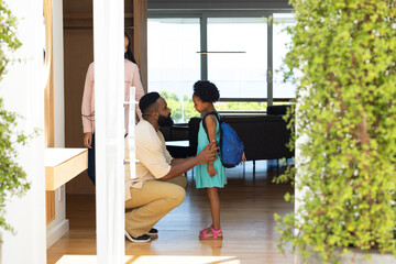 Father kneeling, encouraging daughter with backpack before school at home entrance